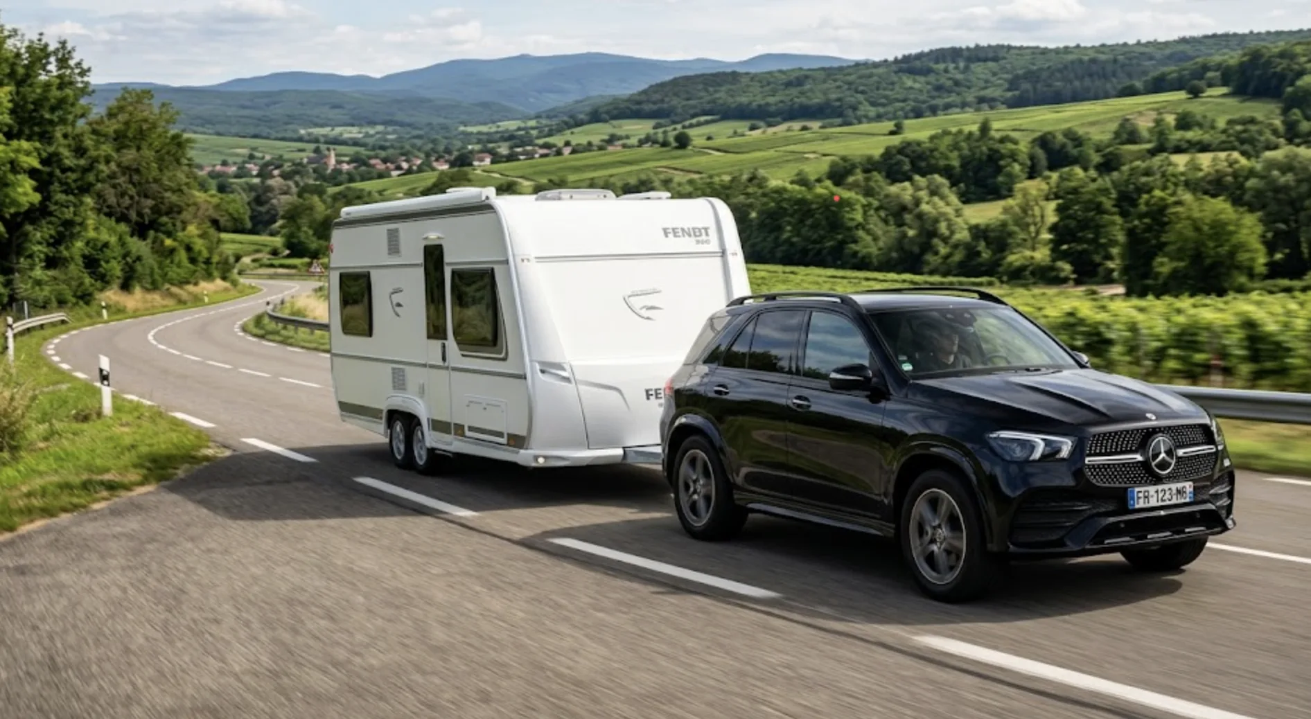 Grand SUV Mercedes sombre tractant une longue caravane blanche double essieu sur une route nationale